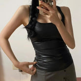 Person wearing a black sleeveless top and gray pants, taking a mirror selfie.